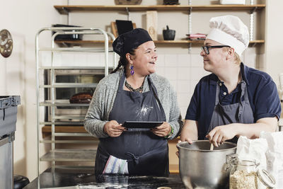 Smiling female baker looking at colleague while baking in kitchen