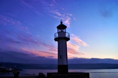 Lighthouse by sea against sky during sunset