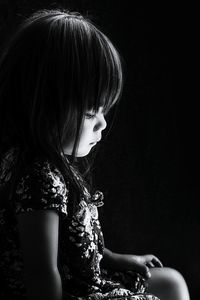 Close-up of young woman sitting against black background