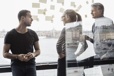 Business colleagues discussing by glass window in office