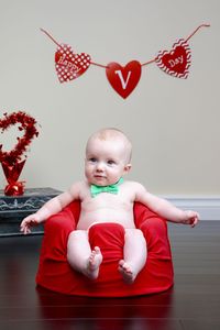 Toddler wearing bow tie sitting on floor seat at home during valentine day