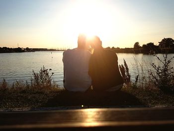 Woman sitting on lake against sky during sunset