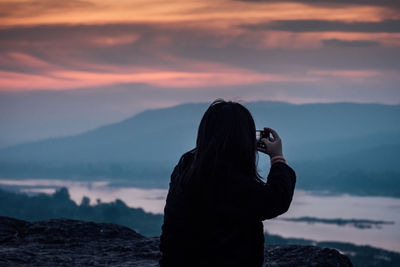 Rear view of woman photographing against sky during sunset