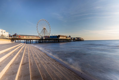 Ferris wheel on a pier in blackpool by sea against sky at sunset