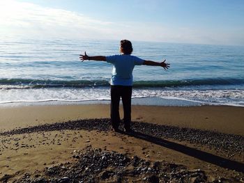 Rear view of woman standing with arms outstretched on shore at beach