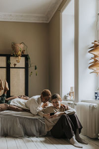 Smiling non-binary couple using mobile phone in bedroom at home