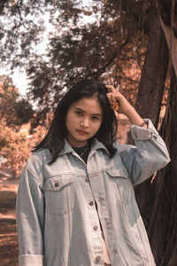 Portrait of beautiful young woman standing against trees