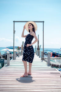Full length portrait of woman standing on pier against sky