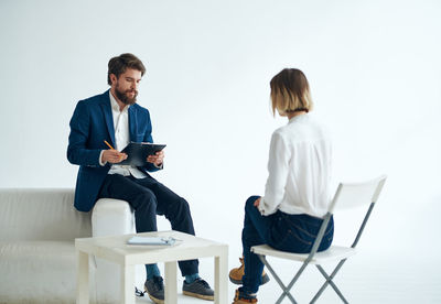 Side view of businessman using digital tablet while sitting against white background