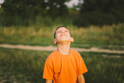 Portrait of a smiling little boy in a orange t-shirt and playing outdoors on the field at sunset