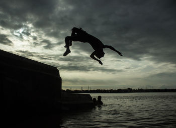 Silhouette man jumping in sea against sky