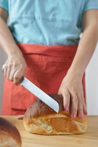 Midsection of woman cutting bread in kitchen