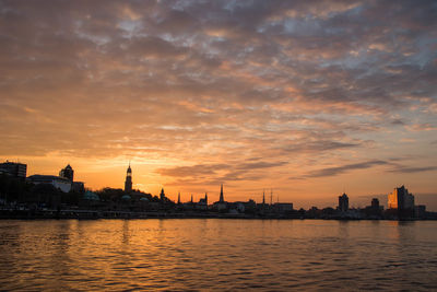 Buildings by river against sky during sunset