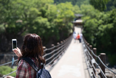 Rear view of woman photographing on footbridge