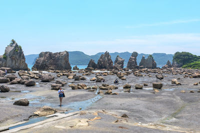 Rear view of woman standing on rock against sky