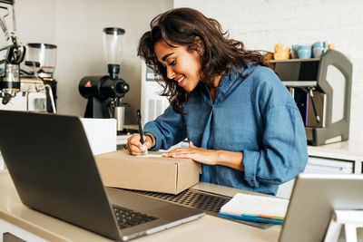 Smiling young woman writing on cardboard box in cafe