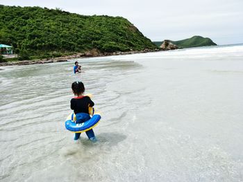 Rear view of girl wearing inflatable ring looking at father on shore