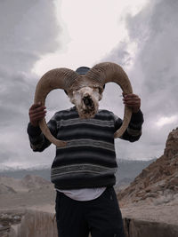 Man holding animal skull while standing on land against sky