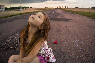 Cute girl looking up while sitting road