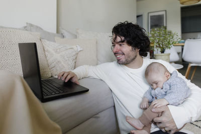 Happy freelancer working on laptop with baby boy sleeping at home