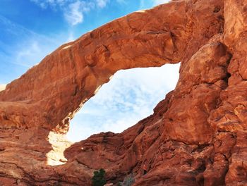 Low angle view of red rock arch against cloudy sky