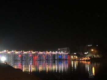 Illuminated city by river against sky at night