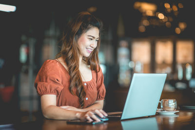 Smiling woman using laptop on table in restaurant