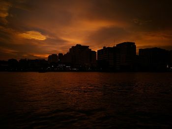 Silhouette city by sea against sky during sunset