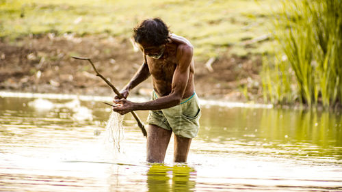 Shirtless man holding stick while standing in lake