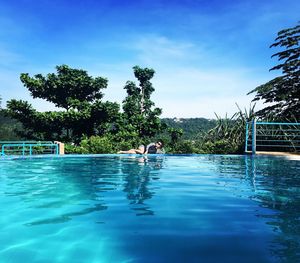 Swimming pool by trees against blue sky