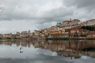 Coimbra university and cityscape by river mondego against sky with reflection