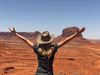 Woman with arms outstretched standing on dirt road against blue sky