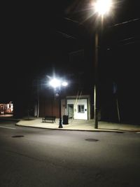 Empty road by illuminated buildings in city at night