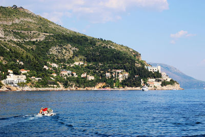 People on sea by mountain against sky