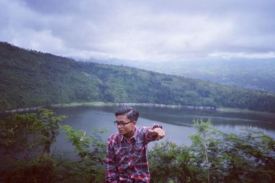 Woman standing in front of lake against cloudy sky