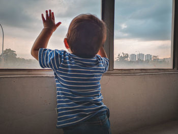 Rear view of boy with arms raised against sky