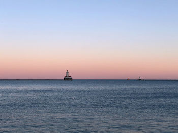 Silhouette lighthouse in sea against clear sky during sunset