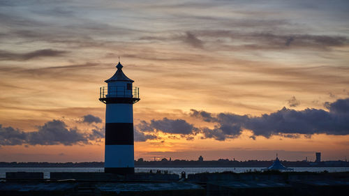 Lighthouse by sea against sky during sunset