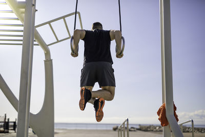 Low angle view of man exercising on gymnastic rings against sky