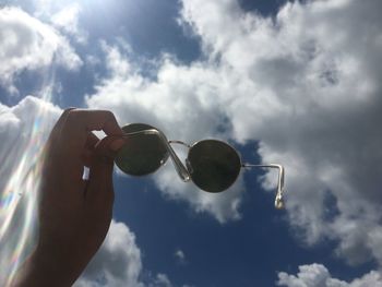 Low angle view of hand holding sunglasses against sky