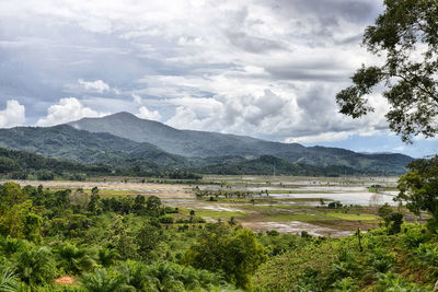 Idyllic shot of green landscape and mountains against cloudy sky