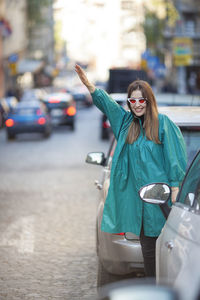 Portrait of smiling woman hailing ride while standing on street in city