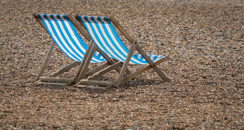 Two blue and white striped deckchairs on a pebble beach