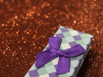 Close-up of christmas gift with purple ribbon on red glittering table