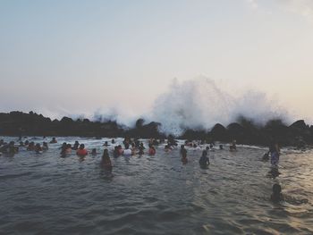 People splashing water in sea against sky during sunset