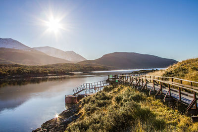 Pier by river against mountains on sunny day