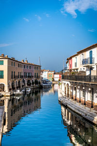 Boats moored on canal by buildings against blue sky