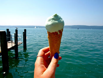 Close-up of hand holding ice cream against sea