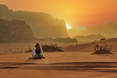 Rear view of man standing at beach against sky during sunset