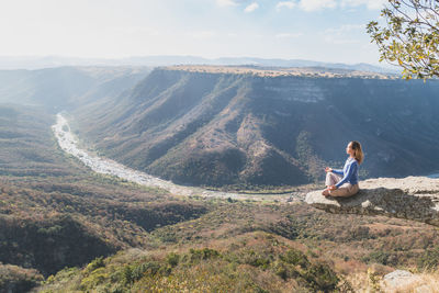 Woman meditating on cliff over mountains at oribi gorge